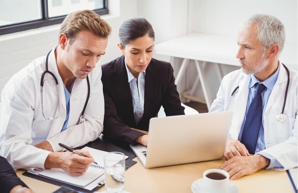 A medical team consults with a healthcare manager in a conference room using a laptop