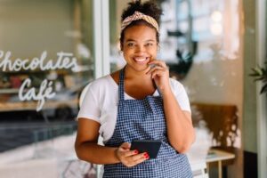 A smiling business owner stands in front of her cafe.