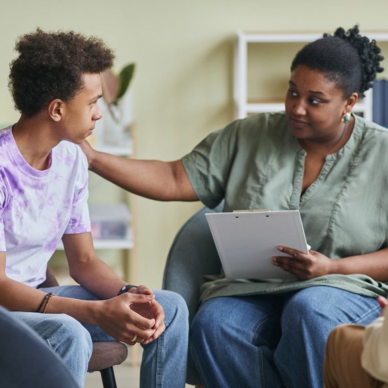 Social Worker talking to teenage boy during therapy session at classroom